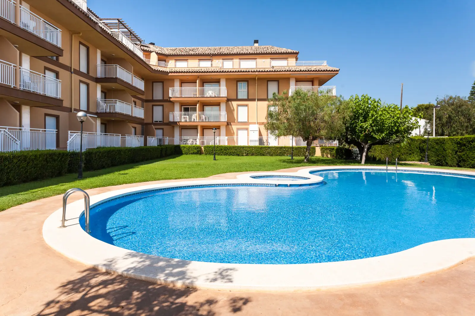 Pool und Garten der Ferienwohnungen Bovalar in Alcossebre mit dem dreistöckigen Gebäude im Hintergrund